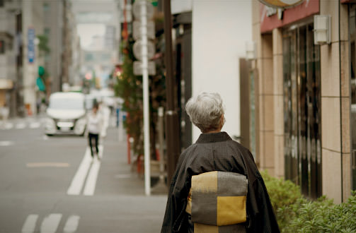 骨董通り周辺の路地を歩く着物姿の女性。古美術店やギャラリーが立ち並ぶ京橋の文化的な街並みを象徴している。