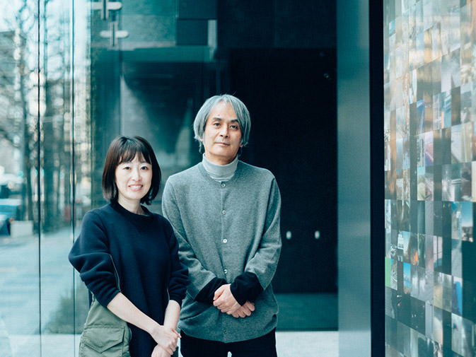 ミュージアムタワー京橋のエントランスにある作品の前に、笑顔の高根枝里氏（左）と落ち着いた表情の高谷史郎氏（右）が並んで立つ写真。高谷史郎氏のインタビュー記事「地球の姿を映したパブリックアート」のサムネイル。